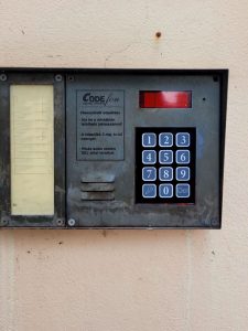 Megkopott, korrodált gombjú analóg codefon kültéri egység betonfalon, Budapest belvárosában.