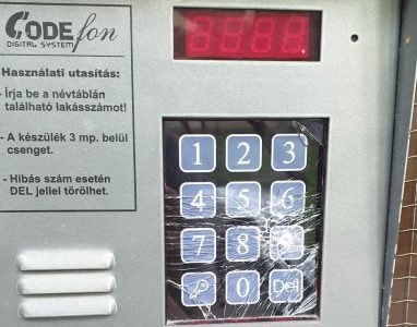 Sárgult, megkopott műanyag burkolatú, régi analóg beltéri kaputelefon-kagyló lakás falán, sérült nyomógombbal.
